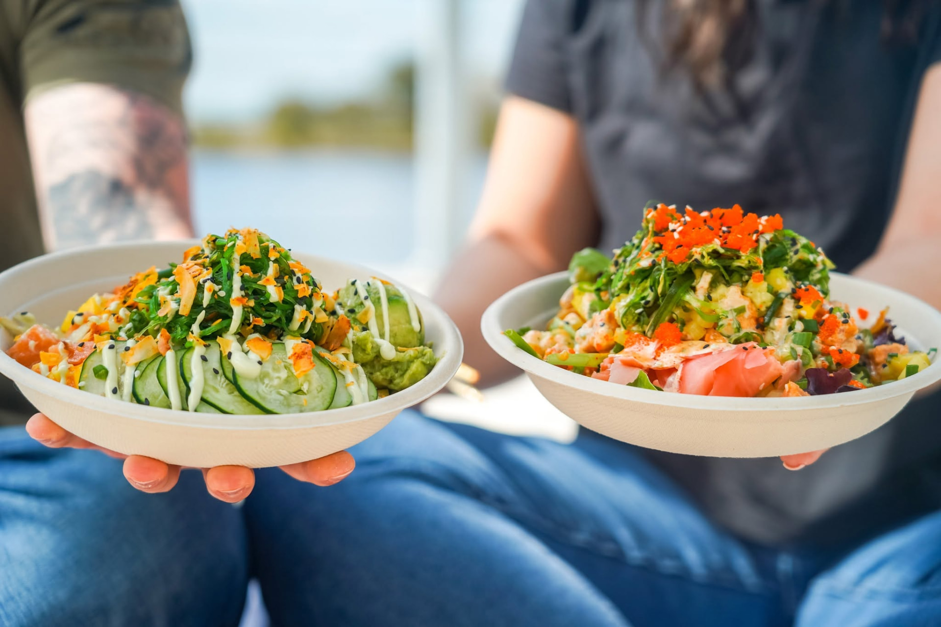 Two guests holding colorful Island Fin Poké bowls at Beachwalk